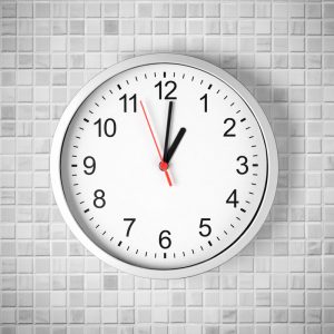 Simple clock or watch on white tile wall displaying one o'clock